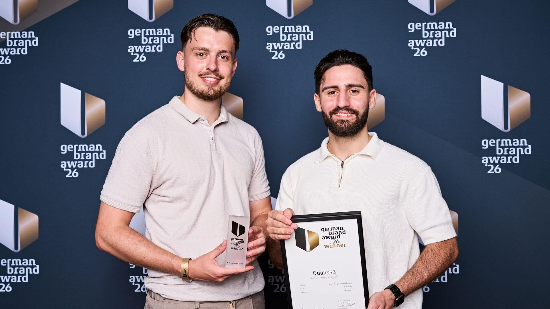 Zwei Beteiligte mit Trophäe und Urkunde für Dualis53 beim German Brand Award 2026