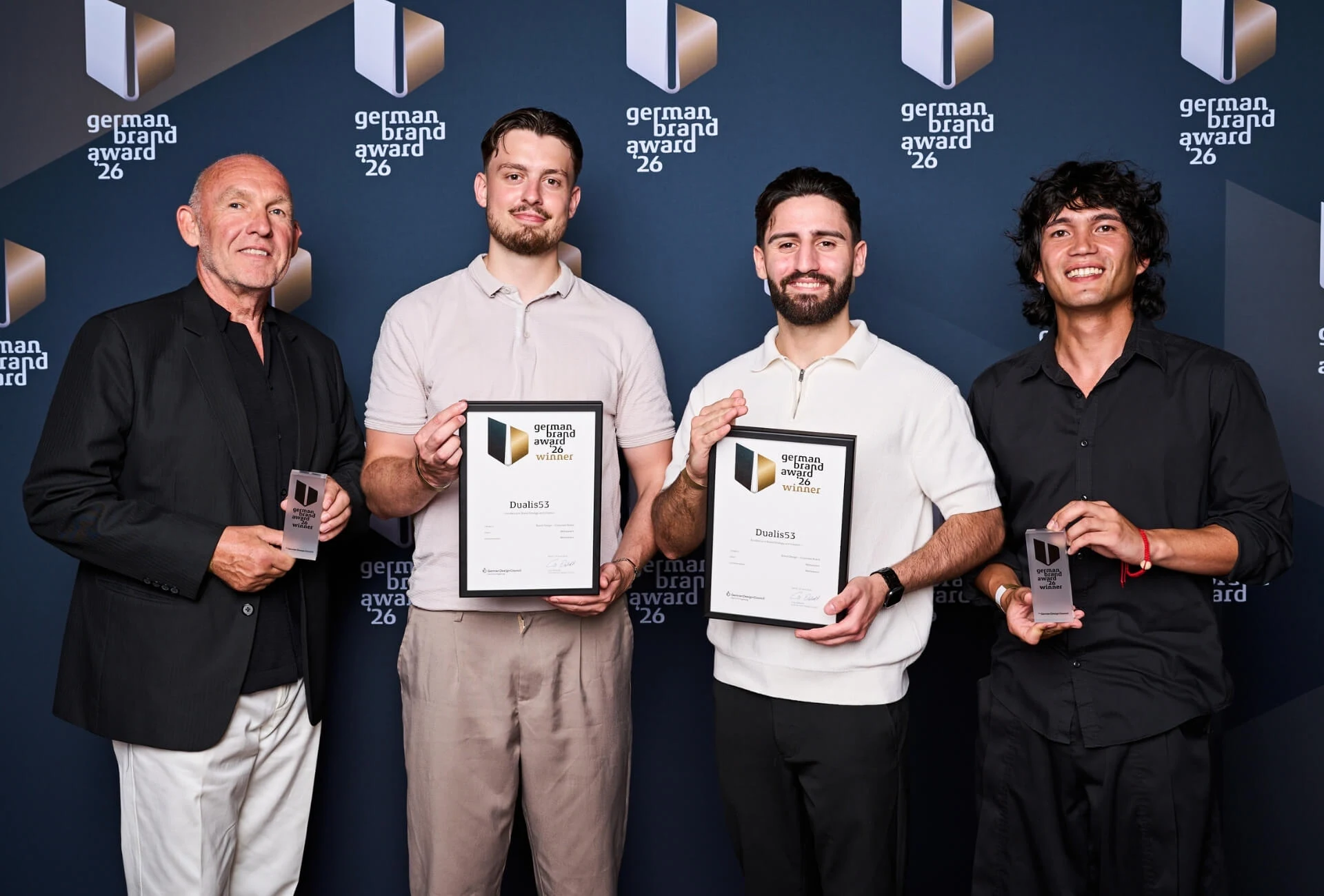 Vier Beteiligte mit Auszeichnungen vor der Fotowand des German Brand Award